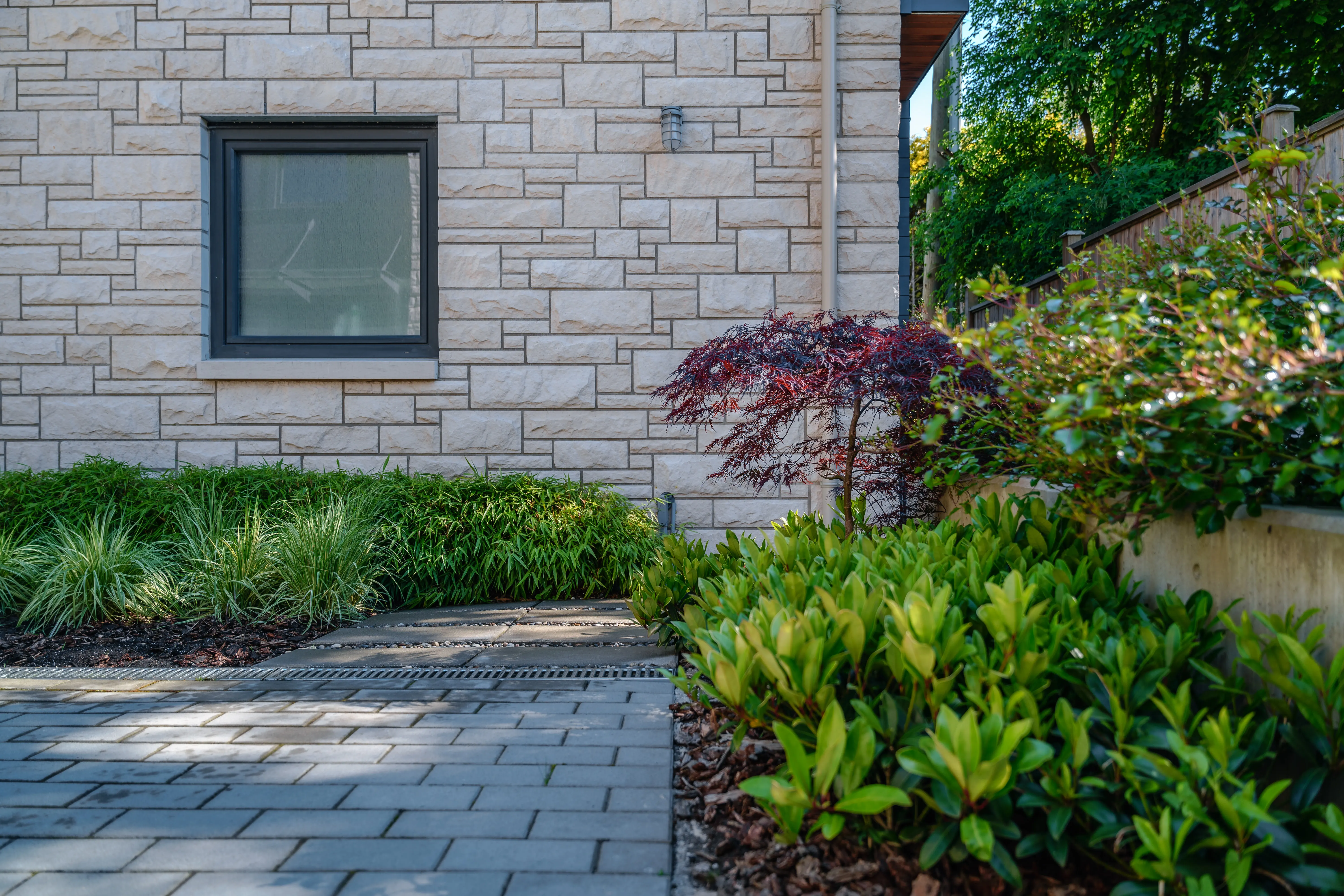 Paver path through shrub planting beside a stone wall at Hudson Street
