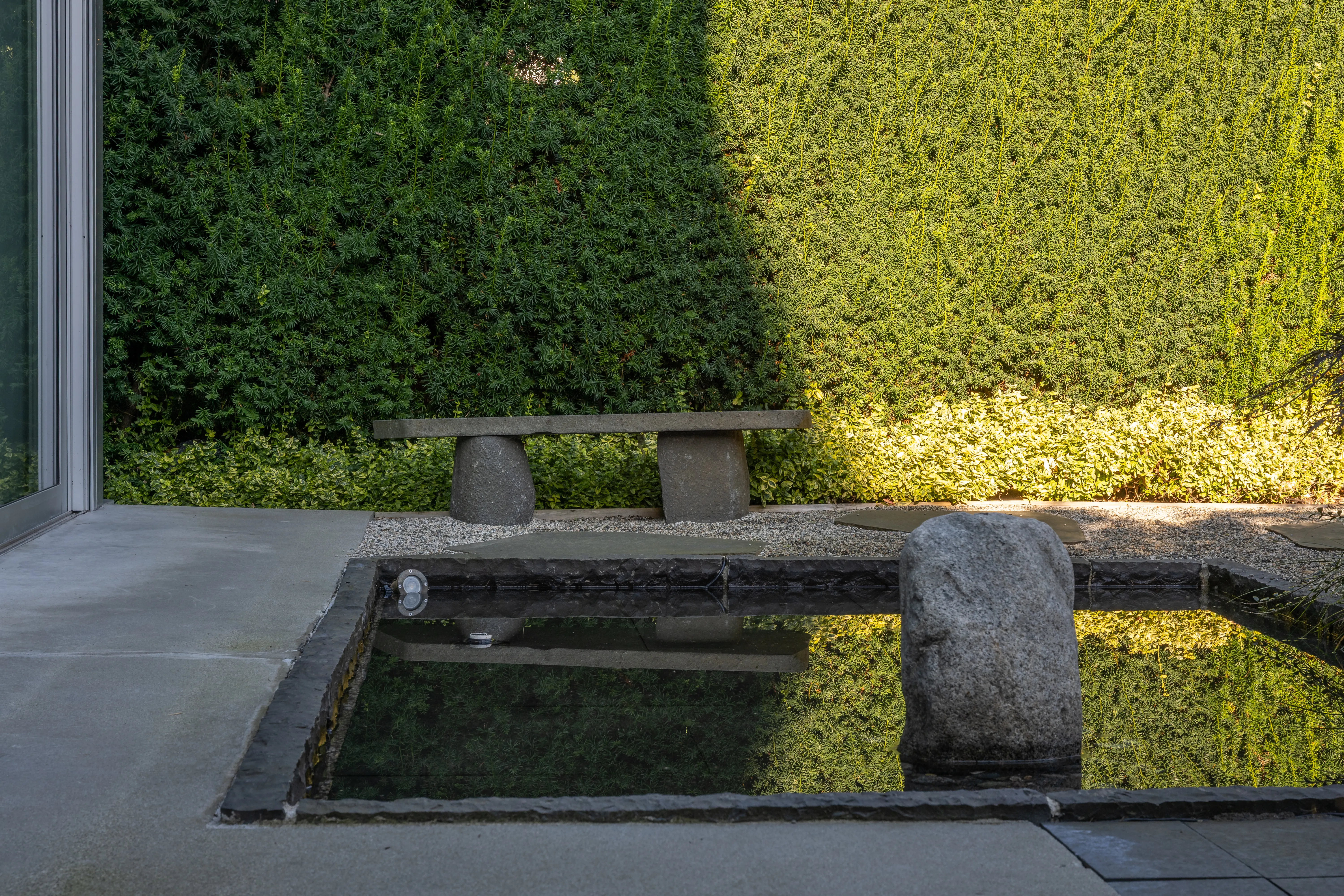 Reflecting pool with boulder and stone bench against a hedge at West 9th
