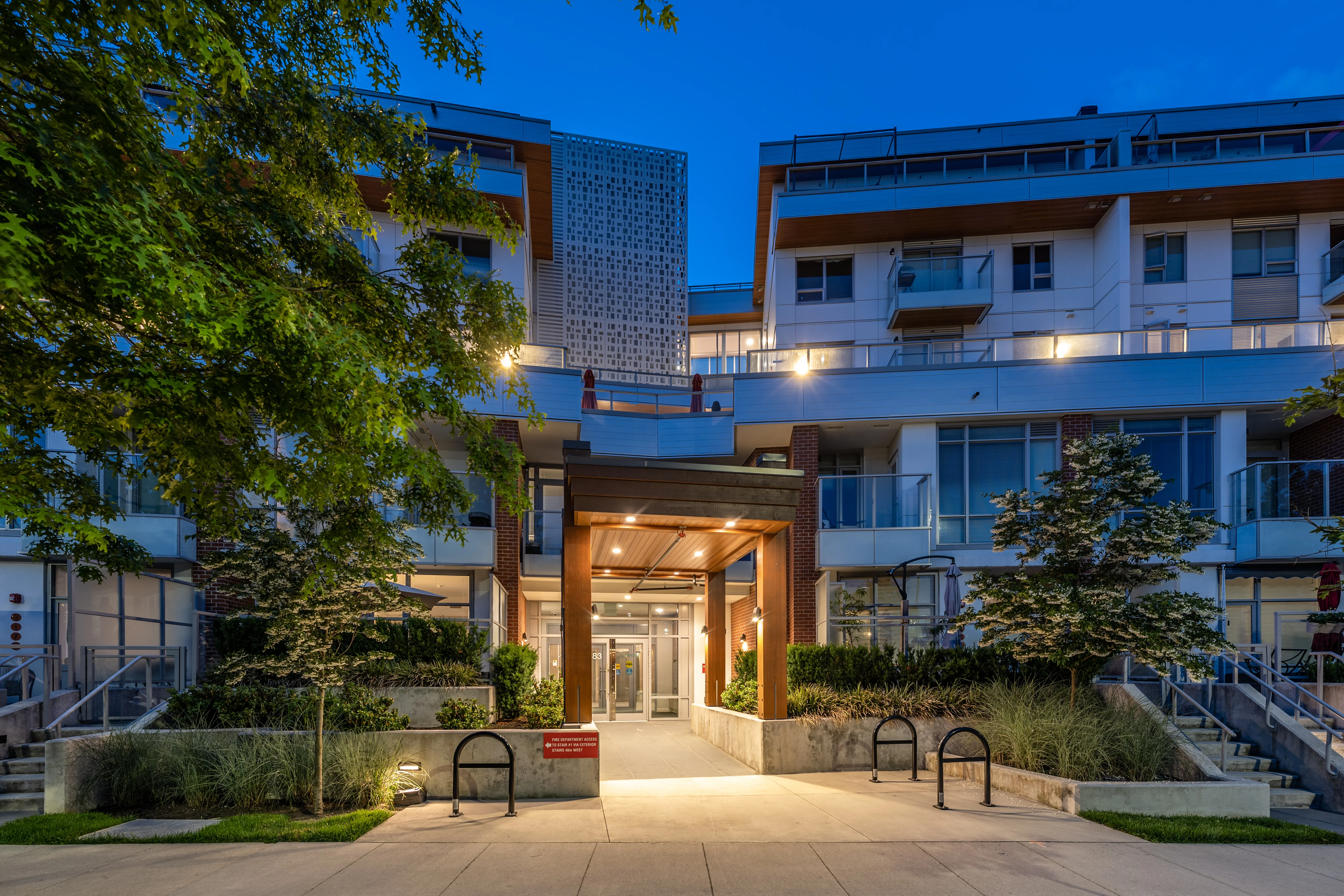 Lit entrance plaza and planting at a residential building at dusk at Kinship