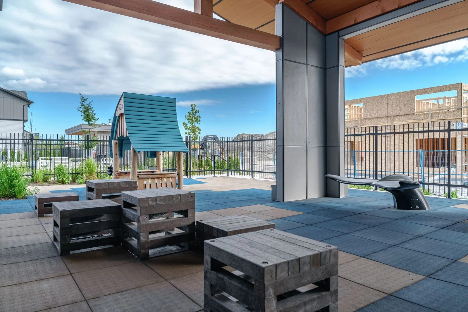 Covered patio with timber seating and a play structure beyond at Boardwalk