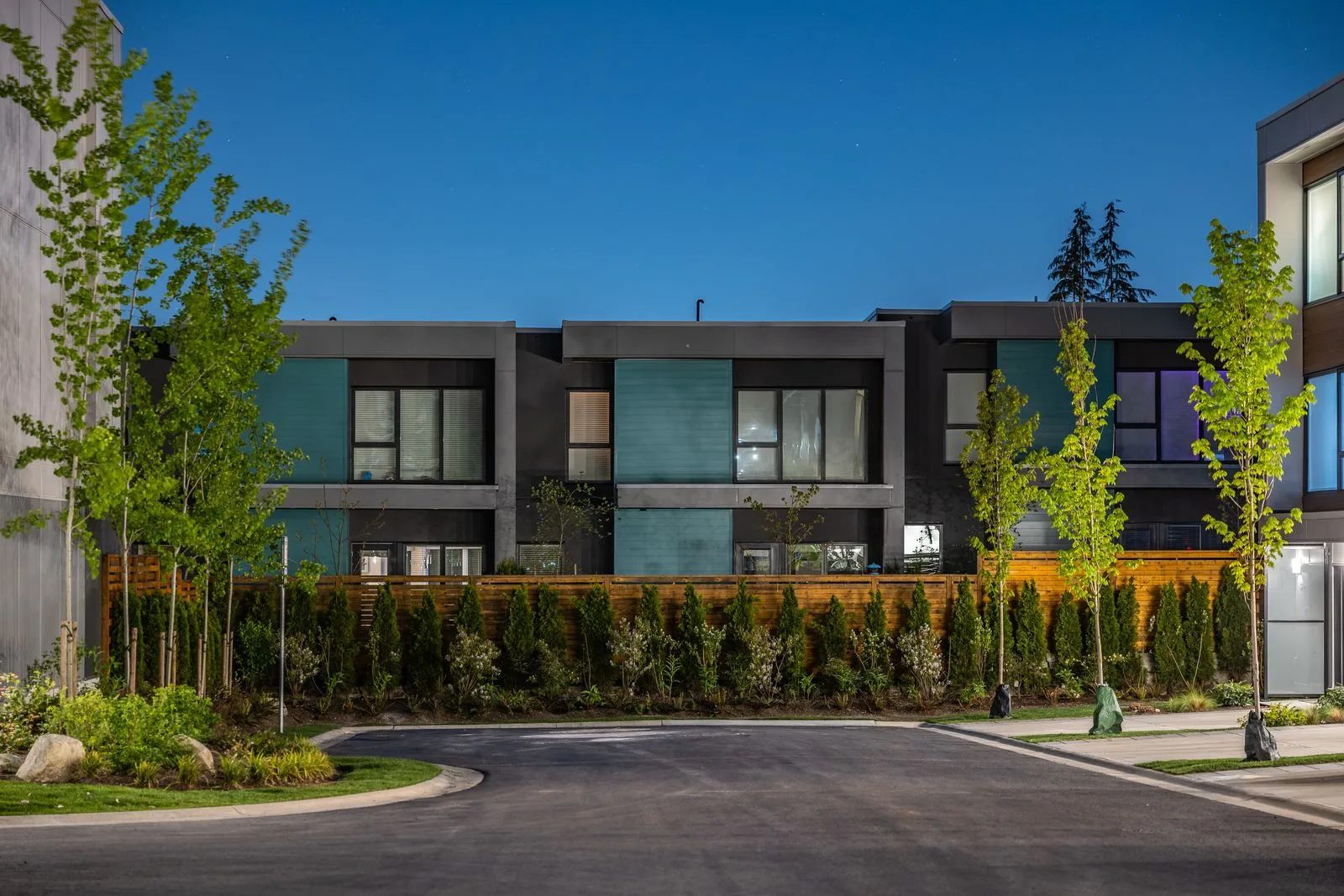Street-side hedges and trees in front of townhomes at dusk at Seymour Village Amenity Park