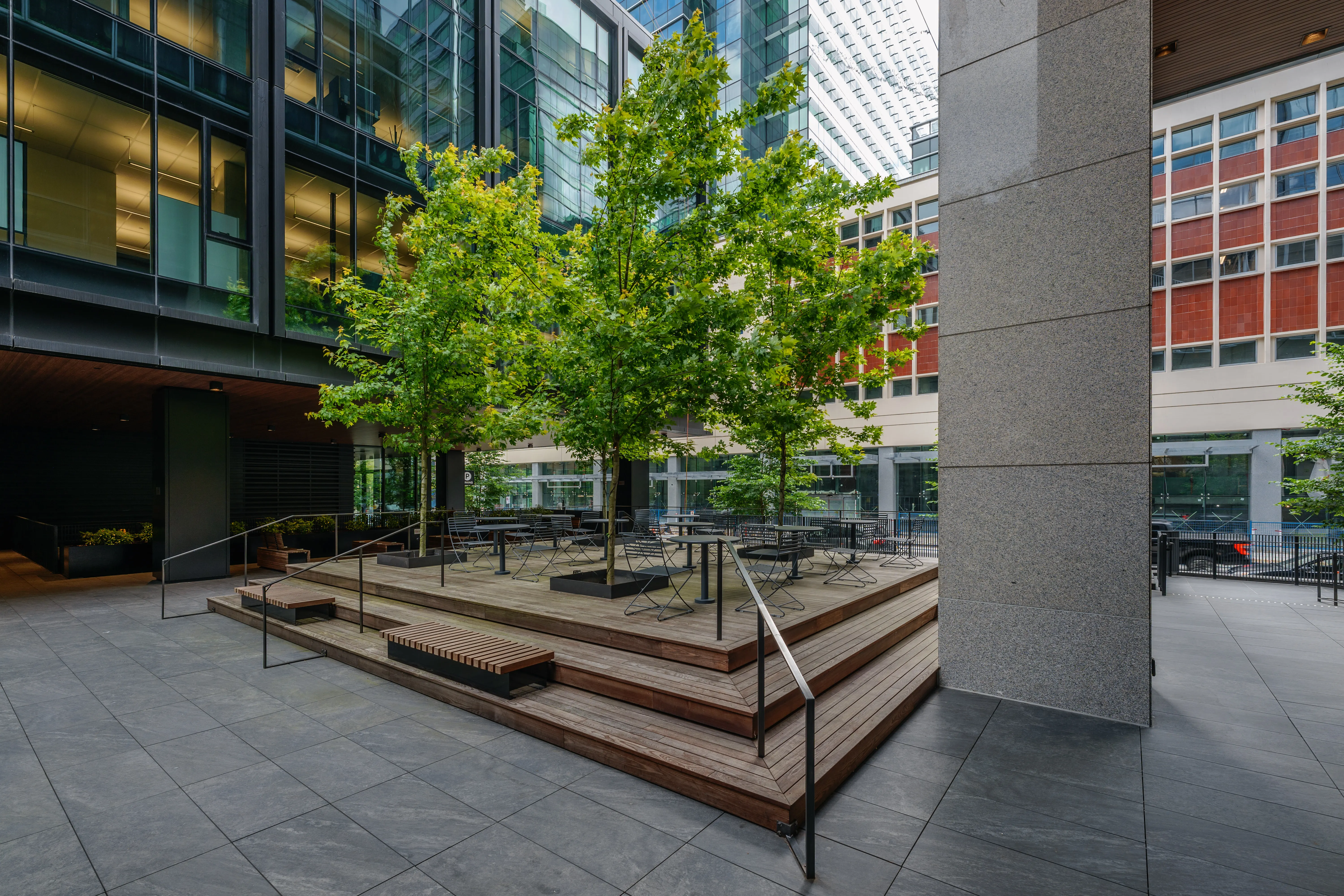 Plaza with timber steps, trees and planters below an office building