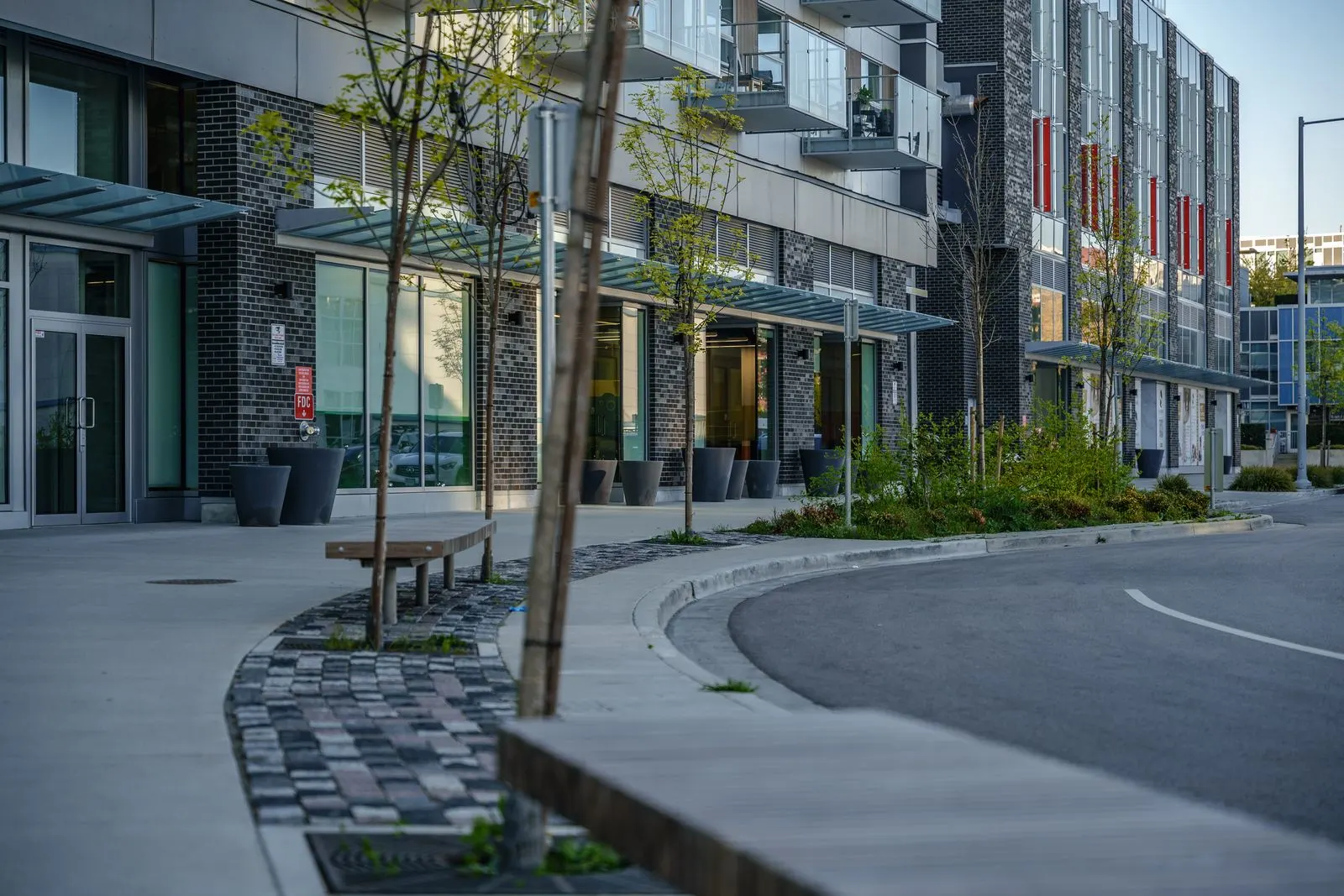 Paved plaza with bench and young tree at a building corner at River Park Place 2