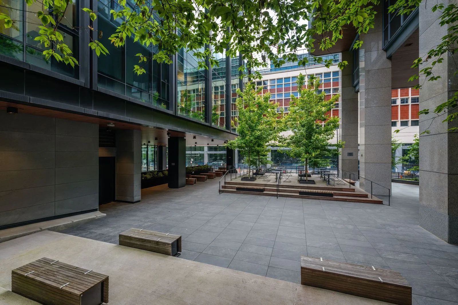 Plaza with timber benches and trees under a building overhang at Amazon Downtown