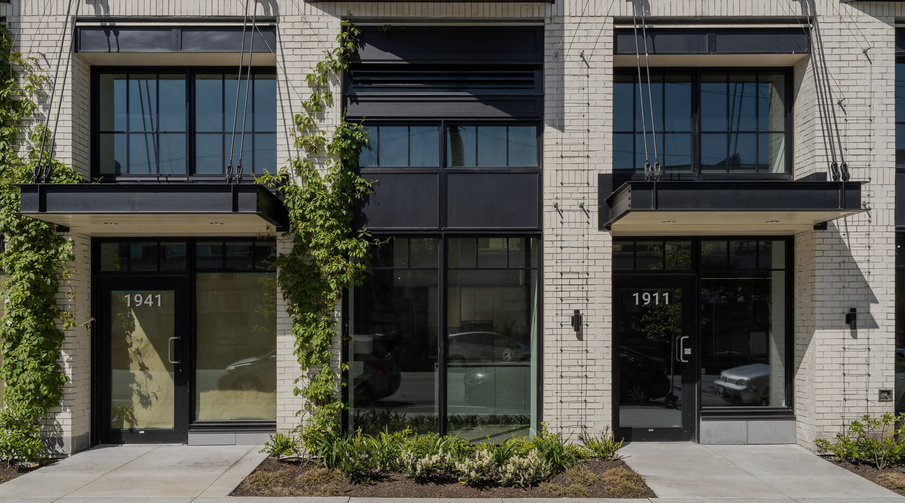 Street-level unit entries with climbing vines and low planting on a brick facade