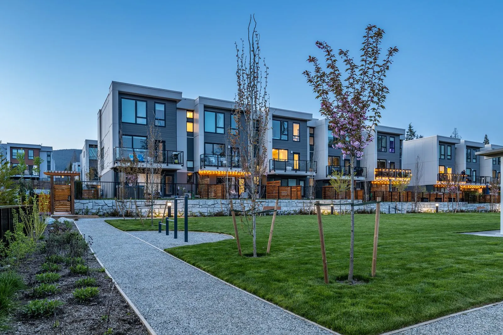 Pathway and lawn with young trees beside townhomes at Seymour Village Amenity Park