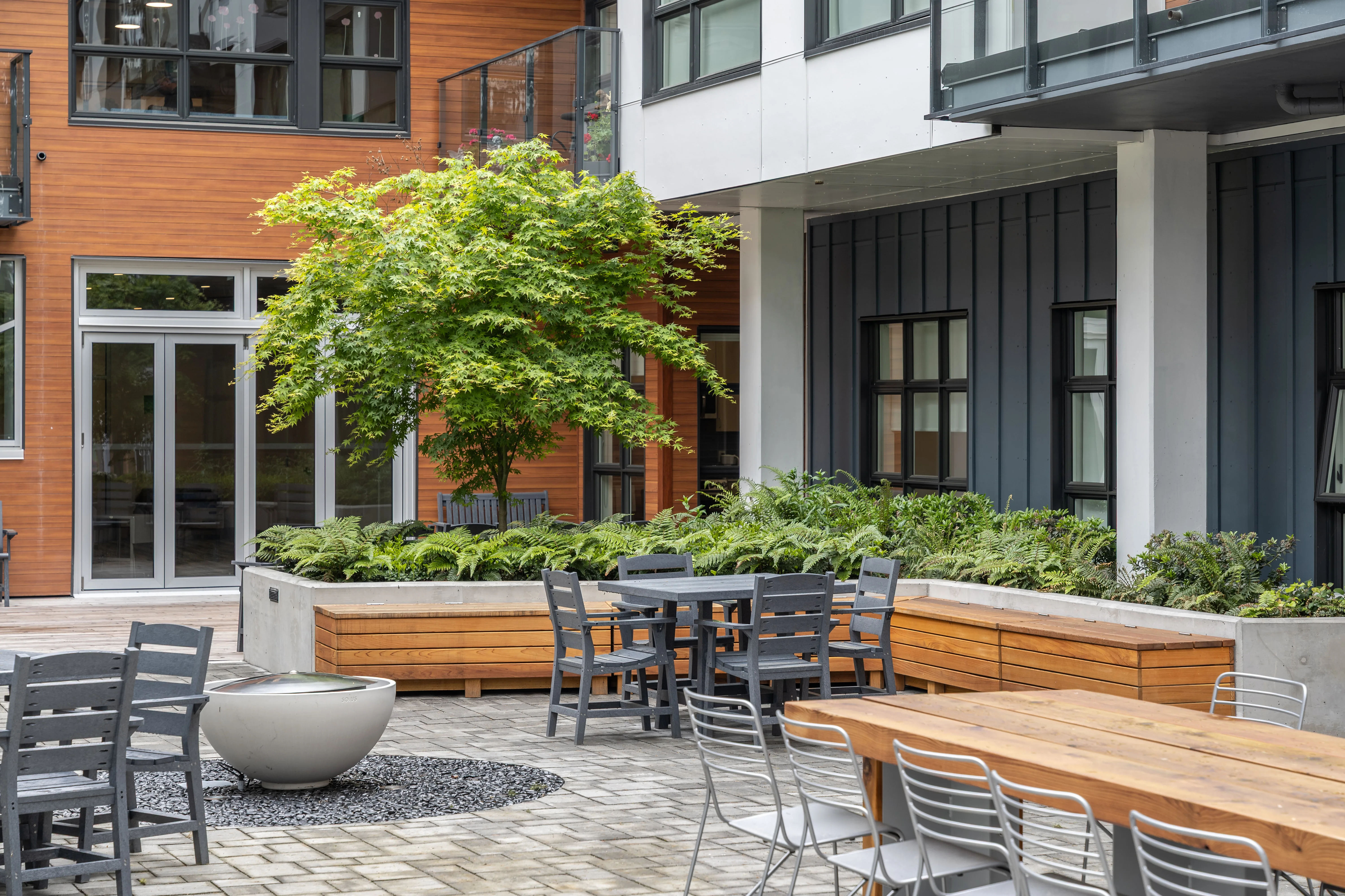 Courtyard dining tables, timber planters and a tree at L'Arche Community Centre