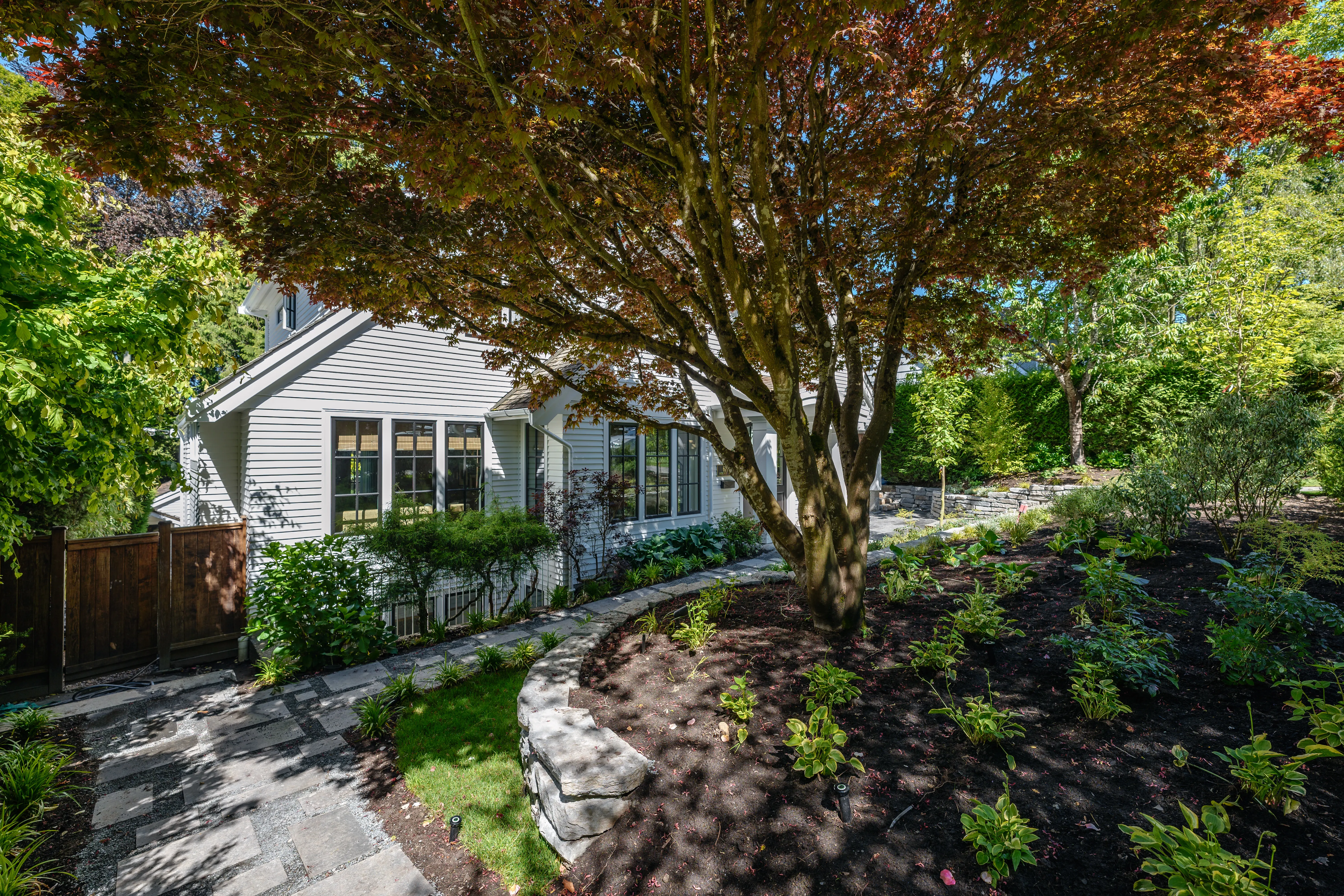 Stone wall and planting beds under a mature tree in a front yard at MacKenzie