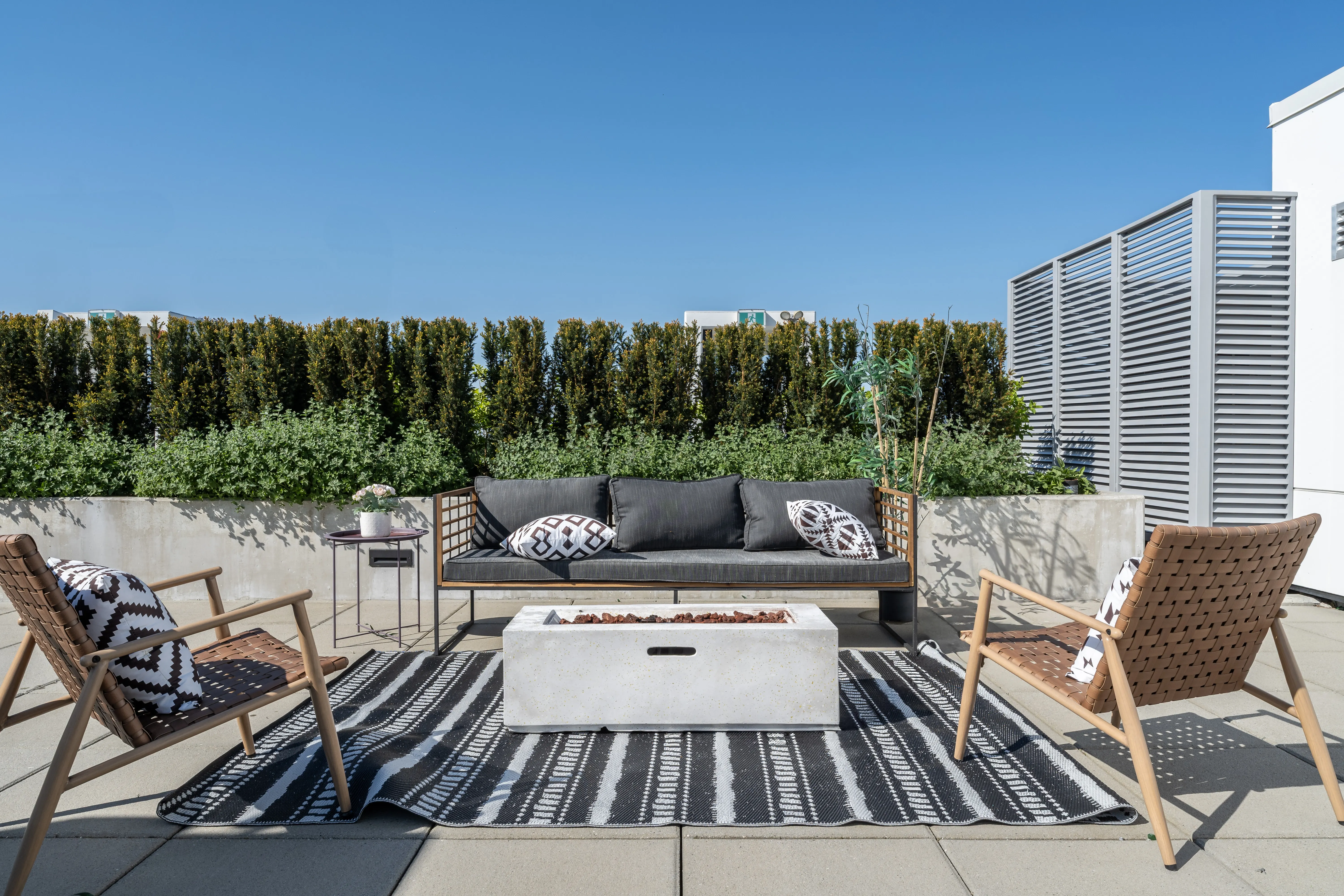 Rooftop lounge seating around a fire table framed by hedges at Voyce