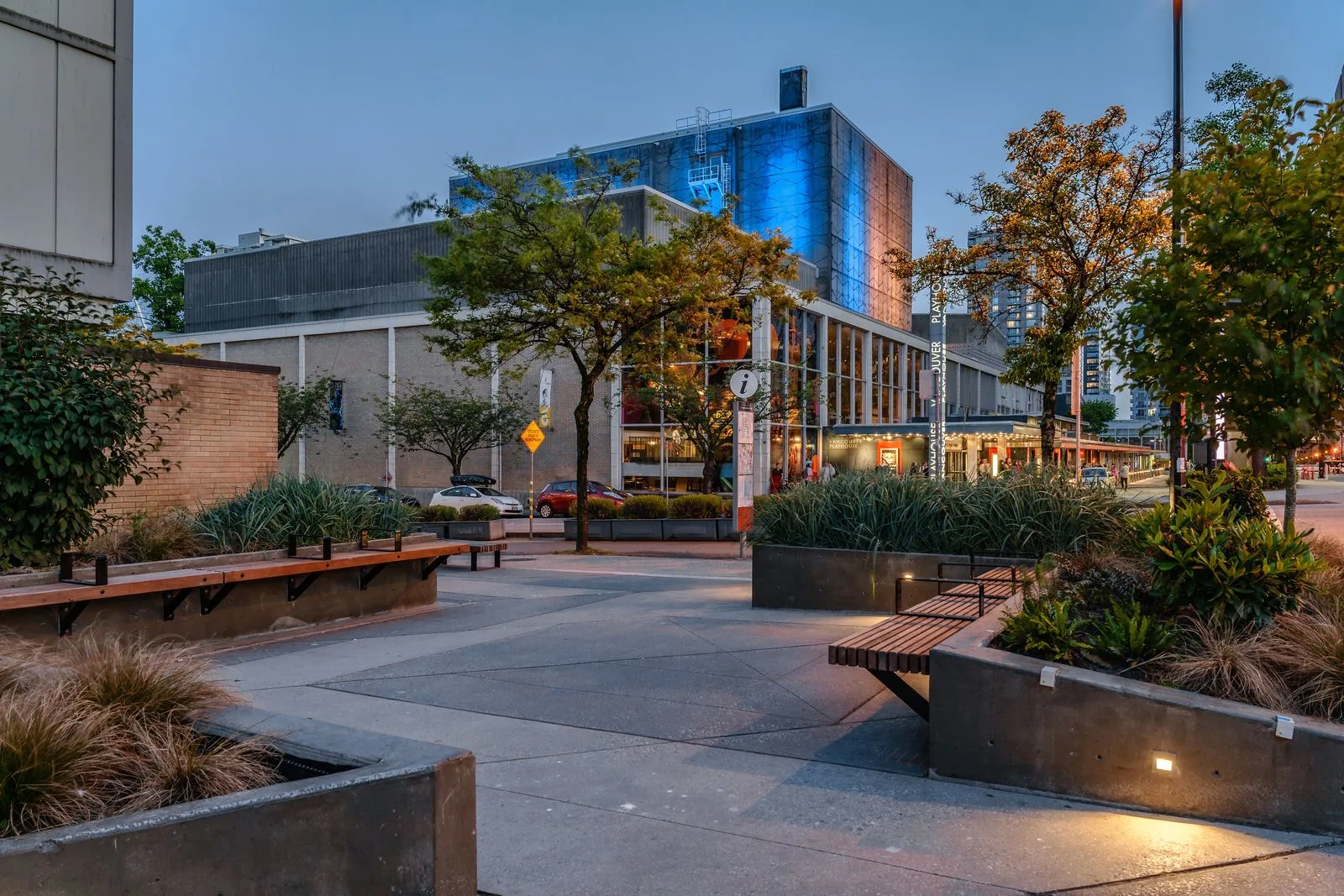 Plaza with timber benches and lit planters at dusk at Vancouver Community College