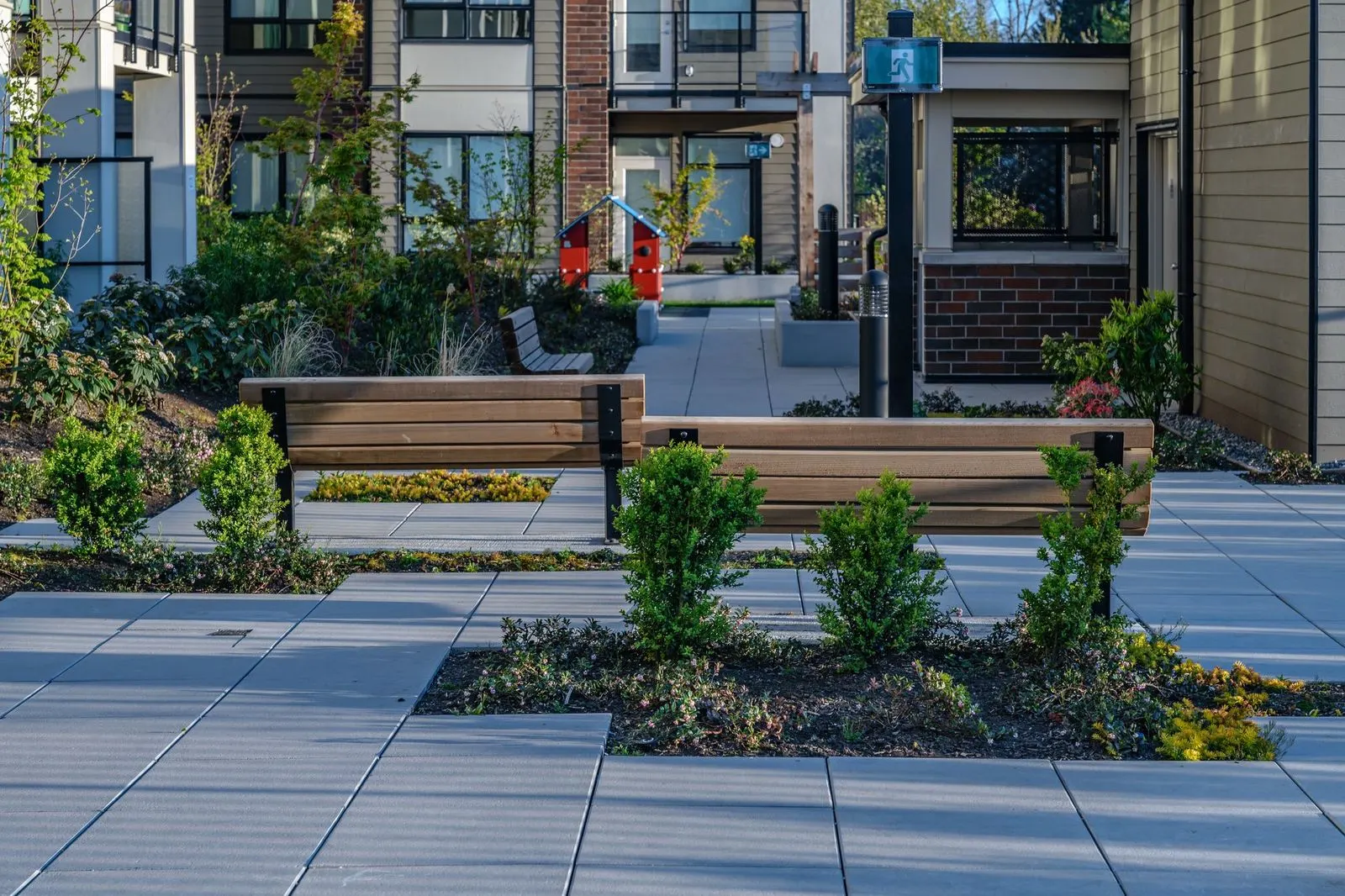 Timber benches and young shrubs in a paved courtyard at Spark