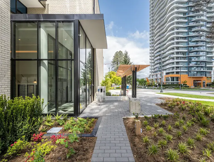 Paver walkway with planted beds beside a glass building entrance